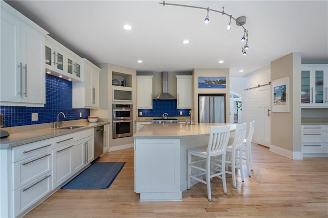 kitchen featuring backsplash, appliances with stainless steel finishes, a sink, light countertops, and wall chimney exhaust hood