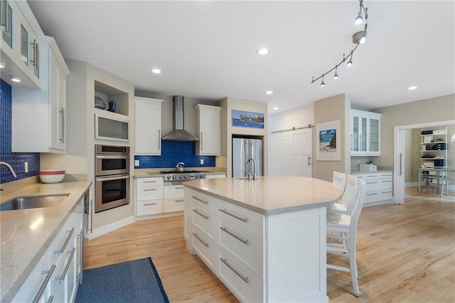 kitchen with wall chimney range hood, appliances with stainless steel finishes, a breakfast bar, a sink, and backsplash