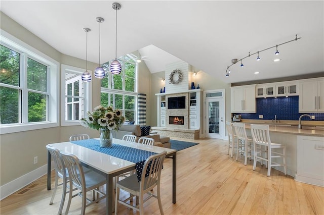dining room with a ceiling fan, a warm lit fireplace, plenty of natural light, and light wood-type flooring