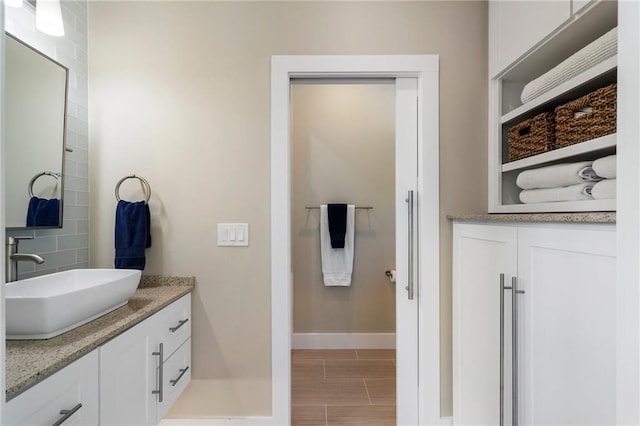 bathroom featuring vanity, wood finish floors, tasteful backsplash, and baseboards