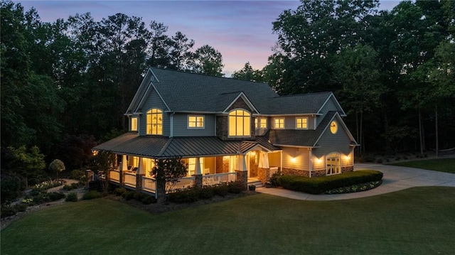 view of front of house with covered porch, a standing seam roof, driveway, a yard, and stone siding