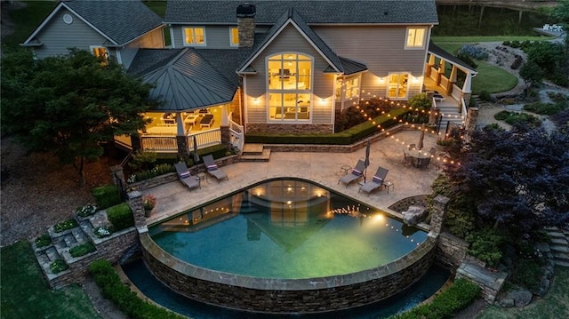 rear view of house with a deck, a patio, a chimney, and an infinity pool