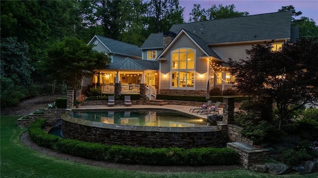 back of property at dusk with a patio, an outdoor pool, and stone siding