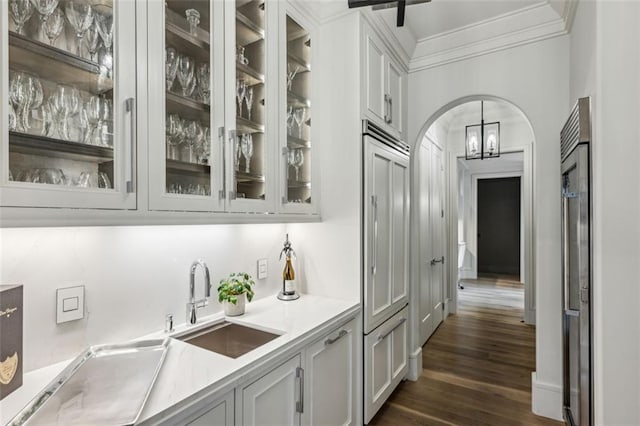 bar with arched walkways, dark wood finished floors, ornamental molding, a sink, and high end fridge