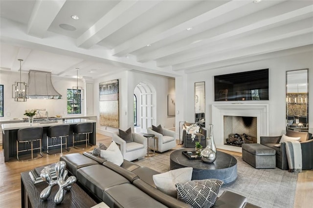 living area featuring a chandelier, beamed ceiling, a fireplace, and light wood-style floors