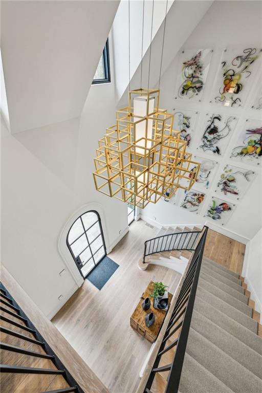 stairs with a towering ceiling, an inviting chandelier, and wood finished floors