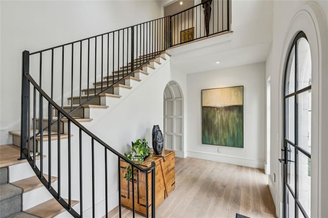 stairway featuring french doors, a high ceiling, wood finished floors, and baseboards