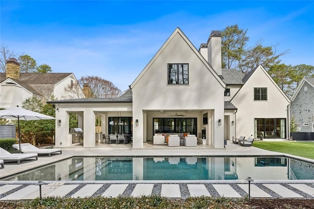 back of property with stucco siding, a chimney, an outdoor living space, and a patio