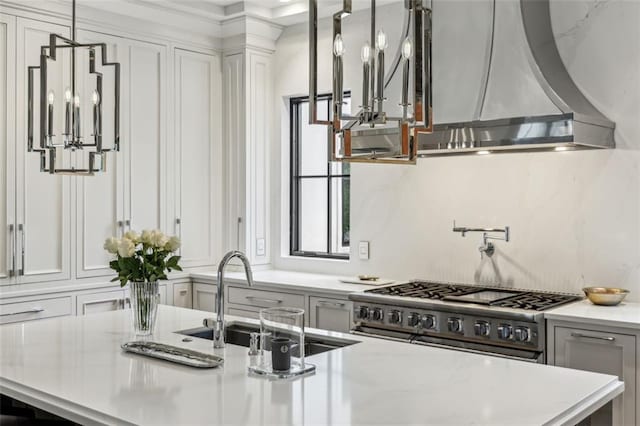 kitchen featuring decorative backsplash, wall chimney exhaust hood, light stone countertops, high end stove, and a sink