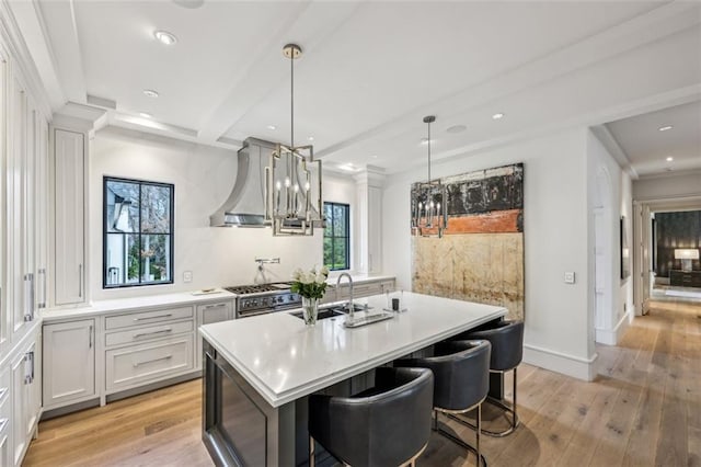 kitchen featuring light wood finished floors, wall chimney exhaust hood, light countertops, and a sink