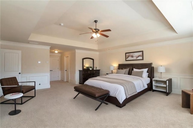 bedroom featuring a wainscoted wall, a raised ceiling, light carpet, and a decorative wall