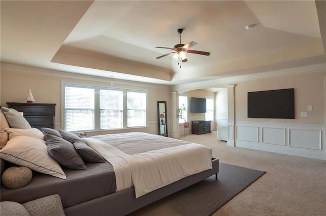 bedroom with light colored carpet, a tray ceiling, a decorative wall, a ceiling fan, and wainscoting