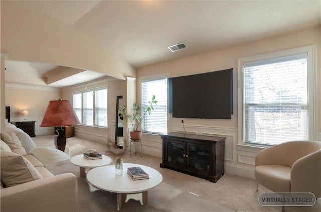 carpeted living room with visible vents, a decorative wall, and wainscoting