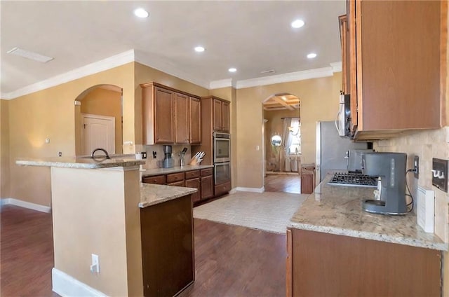 kitchen featuring appliances with stainless steel finishes, dark wood-type flooring, light stone counters, decorative backsplash, and kitchen peninsula