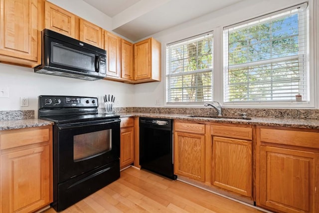 kitchen featuring light wood-style flooring, light stone countertops, black appliances, and a sink