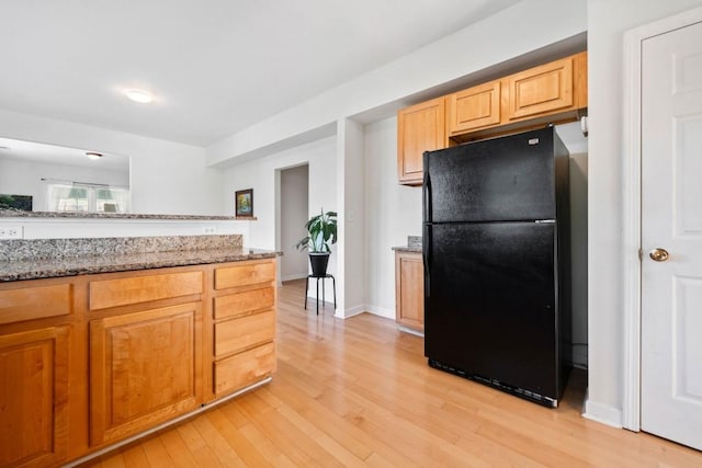 kitchen featuring light stone counters, baseboards, light wood-type flooring, and freestanding refrigerator