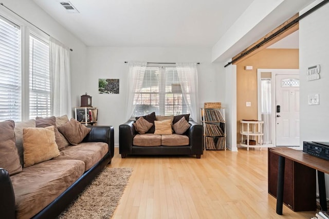 living room featuring a barn door, baseboards, visible vents, and light wood-style flooring