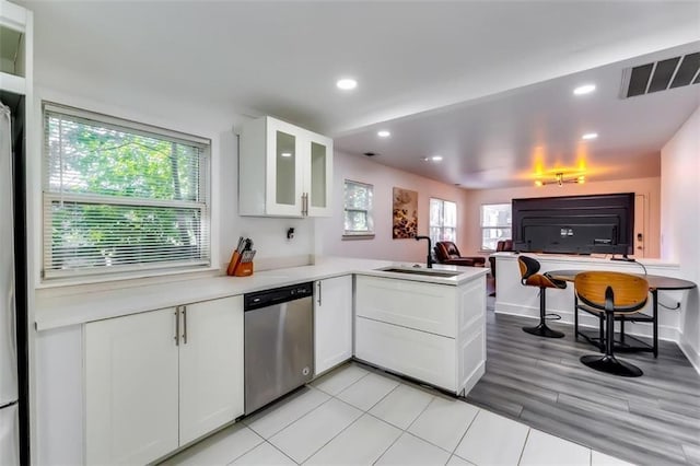 kitchen with sink, light wood-type flooring, dishwasher, kitchen peninsula, and white cabinets