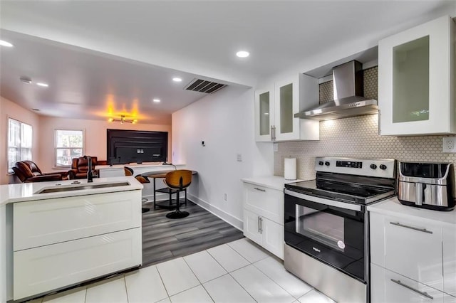 kitchen featuring wall chimney range hood, stainless steel electric range, sink, and white cabinets