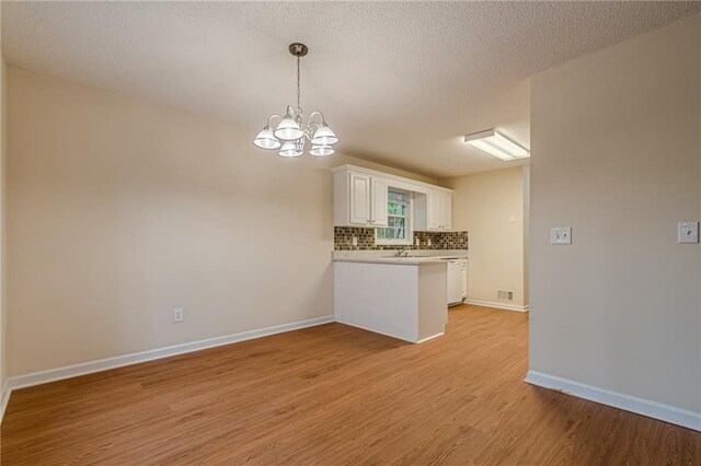 kitchen featuring decorative backsplash, light hardwood / wood-style flooring, a notable chandelier, white cabinets, and a textured ceiling