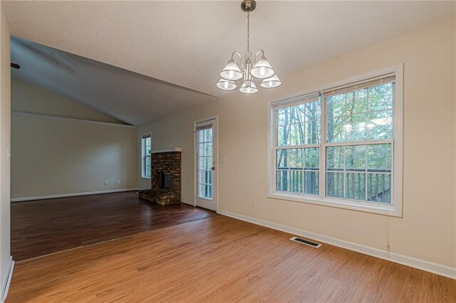 unfurnished living room with wood-type flooring, vaulted ceiling, a chandelier, and a fireplace