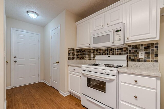 kitchen with decorative backsplash, white cabinets, light hardwood / wood-style flooring, and white appliances