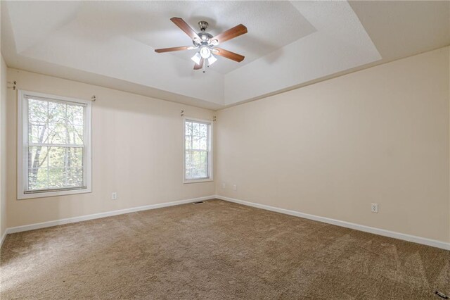 empty room with ceiling fan, carpet, and a raised ceiling