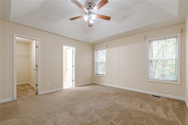 unfurnished bedroom with multiple windows, a spacious closet, ceiling fan, and a raised ceiling