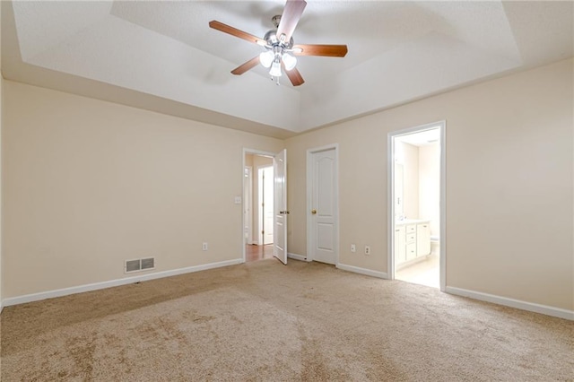 empty room with light carpet, a tray ceiling, and ceiling fan