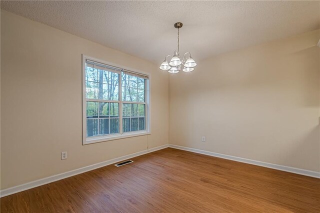 empty room with a notable chandelier, hardwood / wood-style floors, and a textured ceiling