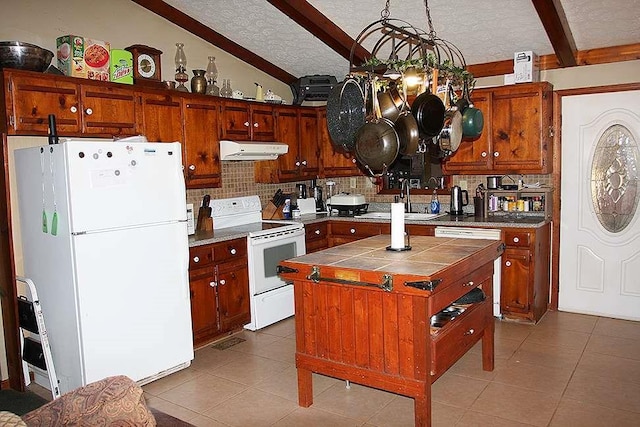 kitchen with white appliances, vaulted ceiling with beams, a center island, a textured ceiling, and tile countertops