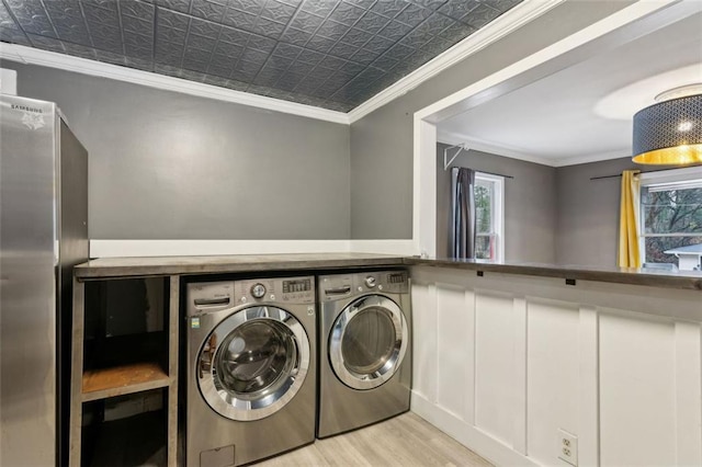 clothes washing area featuring ornamental molding, washing machine and dryer, and light hardwood / wood-style flooring