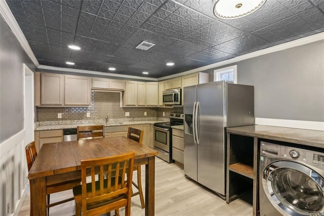 kitchen featuring appliances with stainless steel finishes, ornamental molding, light hardwood / wood-style floors, washer / clothes dryer, and decorative backsplash