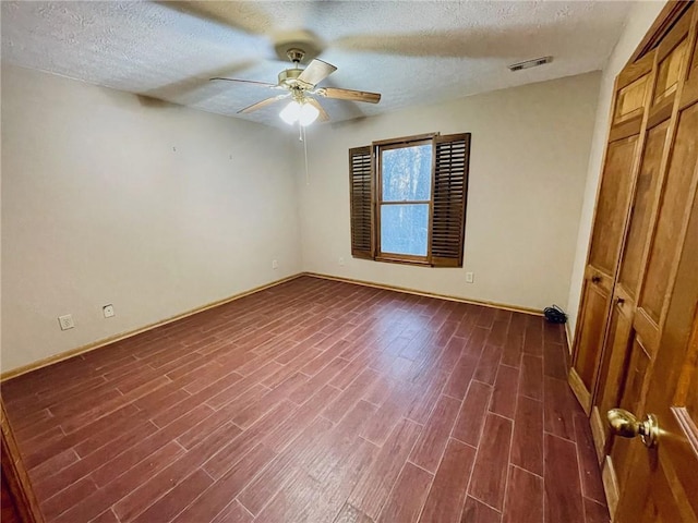 unfurnished bedroom with a textured ceiling, a ceiling fan, baseboards, dark wood-type flooring, and visible vents
