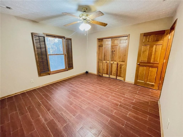 unfurnished bedroom featuring a textured ceiling, visible vents, dark wood finished floors, baseboards, and a closet