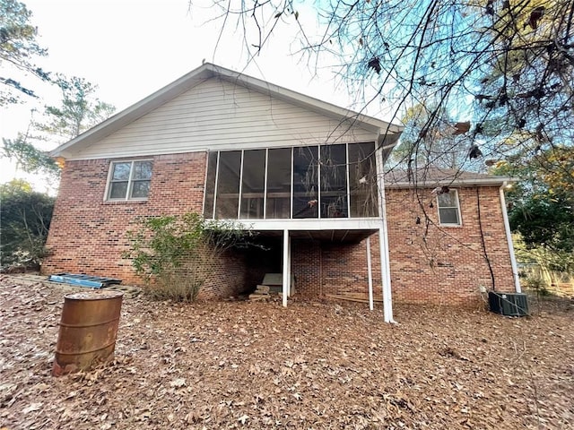 rear view of property with central AC unit, a sunroom, and brick siding