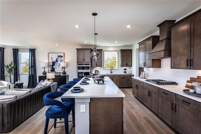 4720 Montane St, Cumming, GA 30028 - kitchen featuring stainless steel appliances, custom exhaust hood, a kitchen breakfast bar, open floor plan, and light wood-style floors