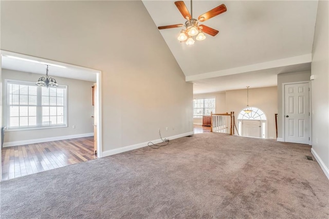 unfurnished living room featuring carpet flooring, ceiling fan with notable chandelier, and high vaulted ceiling