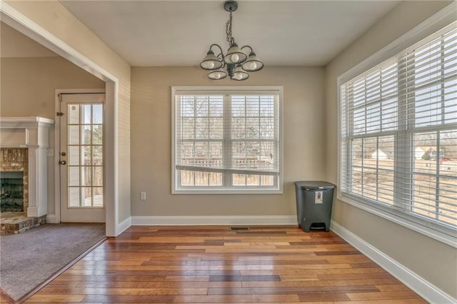 unfurnished dining area with a brick fireplace, a notable chandelier, and light hardwood / wood-style floors