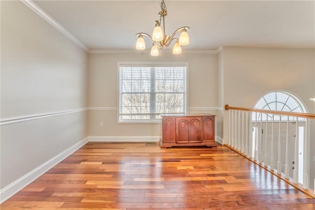 empty room featuring ornamental molding, a chandelier, and light wood-type flooring