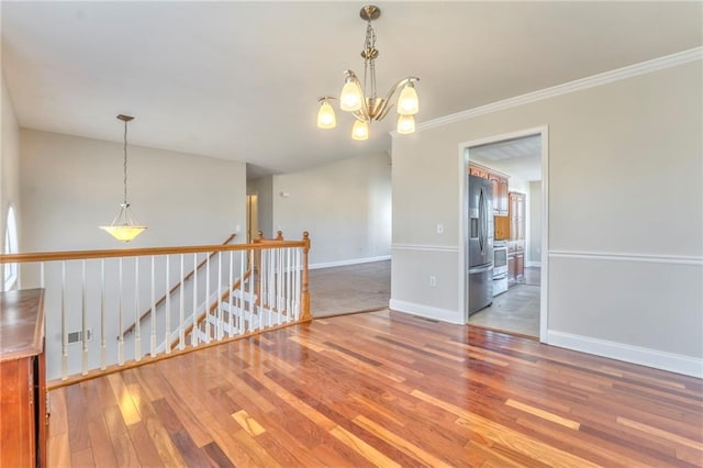 spare room with hardwood / wood-style flooring, crown molding, and an inviting chandelier