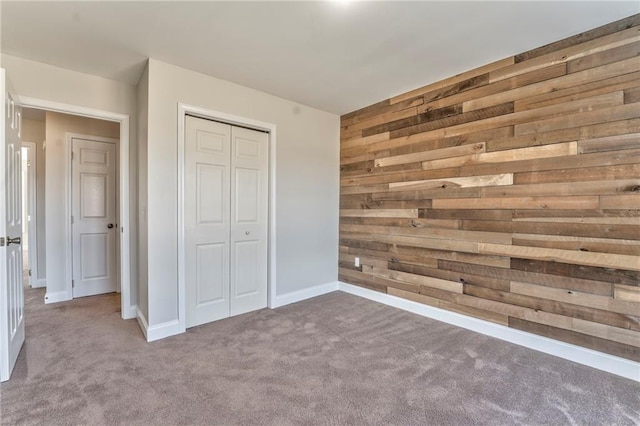 unfurnished bedroom with carpet flooring, a closet, and wood walls