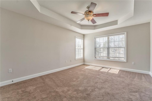 carpeted empty room with a raised ceiling and ceiling fan