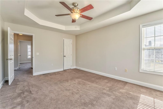 empty room featuring light carpet, a raised ceiling, and ceiling fan