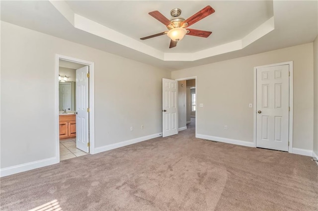 unfurnished bedroom featuring a raised ceiling, ensuite bathroom, and light colored carpet