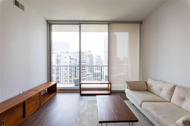 living room featuring dark wood-type flooring, a wall of windows, visible vents, and a city view