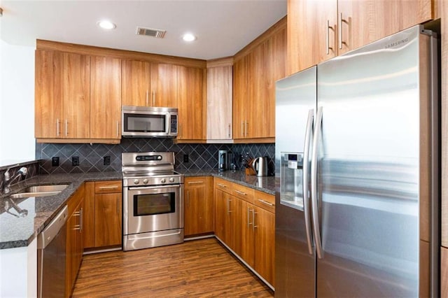 kitchen with dark stone countertops, appliances with stainless steel finishes, brown cabinets, and a sink