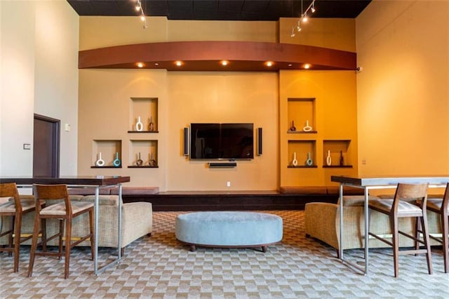 living room featuring a towering ceiling, built in shelves, and track lighting