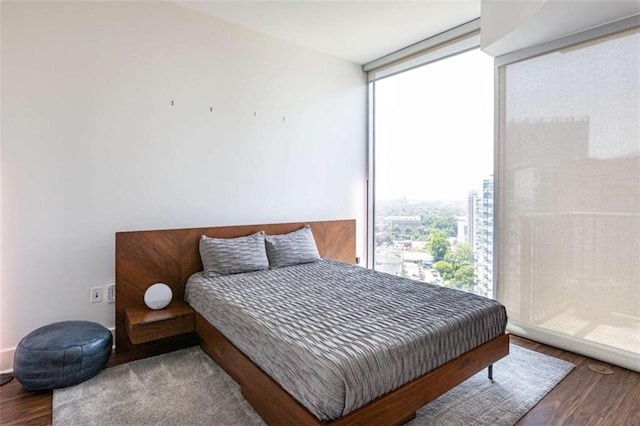 bedroom featuring a view of city, floor to ceiling windows, and wood finished floors