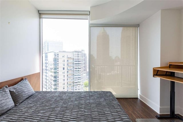 bedroom with a view of city, dark wood-type flooring, a wall of windows, and baseboards